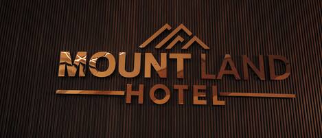 A wooden textured wall with the words "MOUNT LAND HOTEL" in a stylized font.