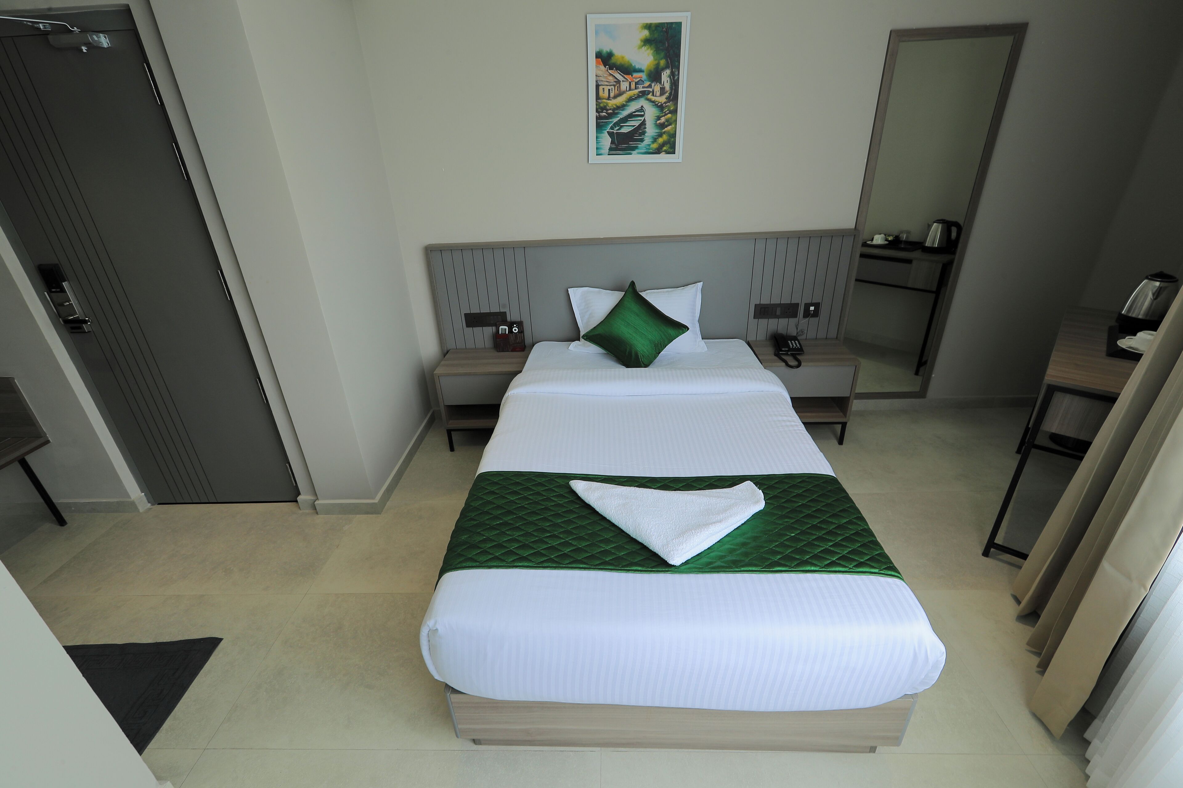Habitación de hotel con cama, mesita de noche, escritorio, silla, un cuadro en la pared y una puerta.