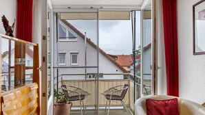 A balcony with a sliding glass door, wicker chairs, a red cushion, and a wooden cabinet.