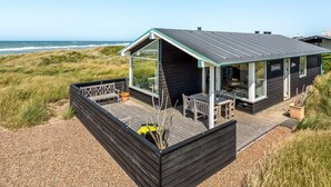 Ein Küstenhaus mit Terrasse, großen Fenstern und Blick auf den Ozean.