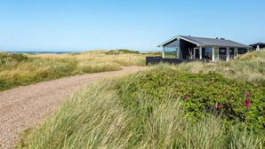 Ein modernes Strandhaus mit einem Kiesweg, umgeben von Dünen und Vegetation.
