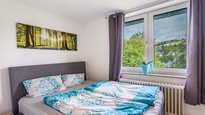 A bedroom with a bed, a window with curtains, a radiator, and a painting on the wall. - 'Apartment by the Park' with Mountain View and Balcony (Willingen (Upland))