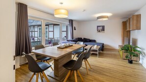 A modern living room with a dining area, wooden flooring, and a large window with curtains. - 'Apartment by the Park' with Mountain View and Balcony (Willingen (Upland))