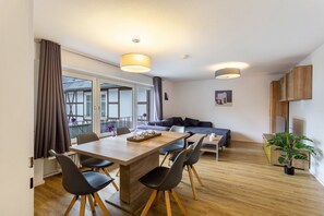 Ein modernes Wohnzimmer mit Essbereich, Holzboden und einem großen Fenster mit Vorhängen.