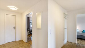 A hallway with wooden flooring, white walls, and a door leading to a room with a bed and a small table. - 'Apartment by the Park' with Mountain View and Balcony (Willingen (Upland))