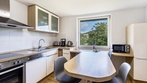 A compact kitchen with a stove, sink, and microwave, a dining table with chairs, and a window with a view of greenery. - 'Apartment by the Park' with Mountain View and Balcony (Willingen (Upland))
