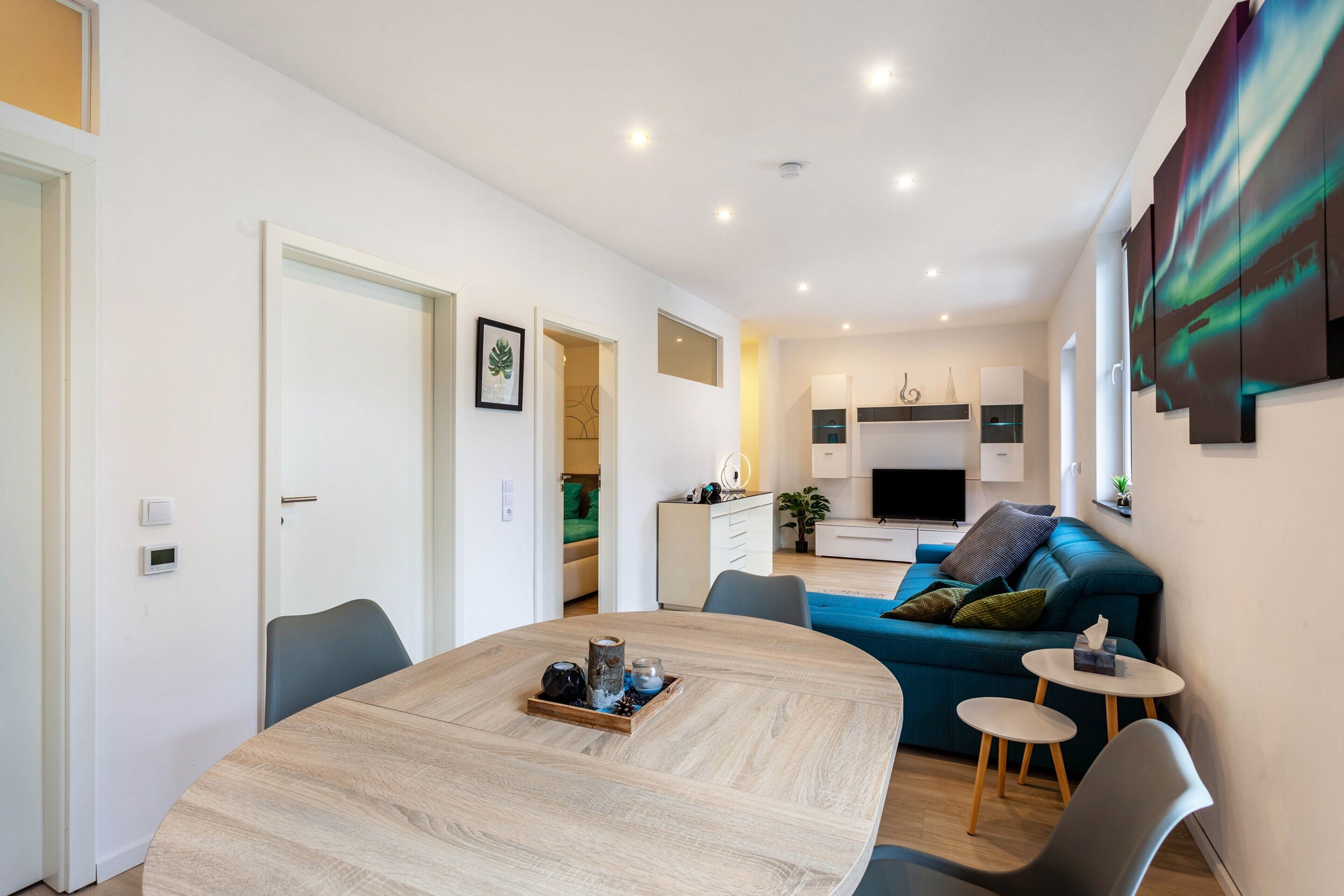 A modern living room with a round dining table, a blue sofa, and a kitchen area in the background.