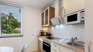 Cocina compacta con horno integrado, microondas y lavaplatos, una mesa de comedor y un ventanal con vistas a zonas verdes.