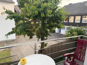 Un balcón con una mesa redonda, una silla roja y un árbol.