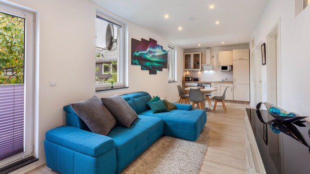 Una sala de estar moderna con un sofá azul, un comedor y una cocina al fondo.