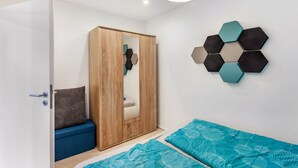 Un dormitorio con un armario de madera, una cama con ropa de cama azul, una lámpara hexagonal fijada a la pared y una puerta con manija.