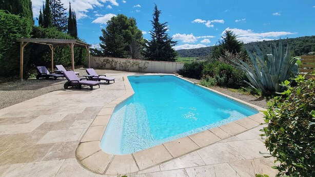 A swimming pool with lounge chairs, surrounded by greenery and a pergola.