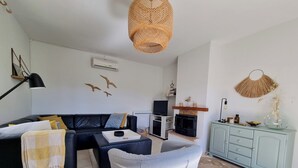 A living room with a black leather sofa, a grey armchair, a wooden stool, a television, a fireplace, a cabinet, and decorative wall art.