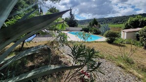 A swimming pool surrounded by greenery, with a view of a hilly landscape in the background.