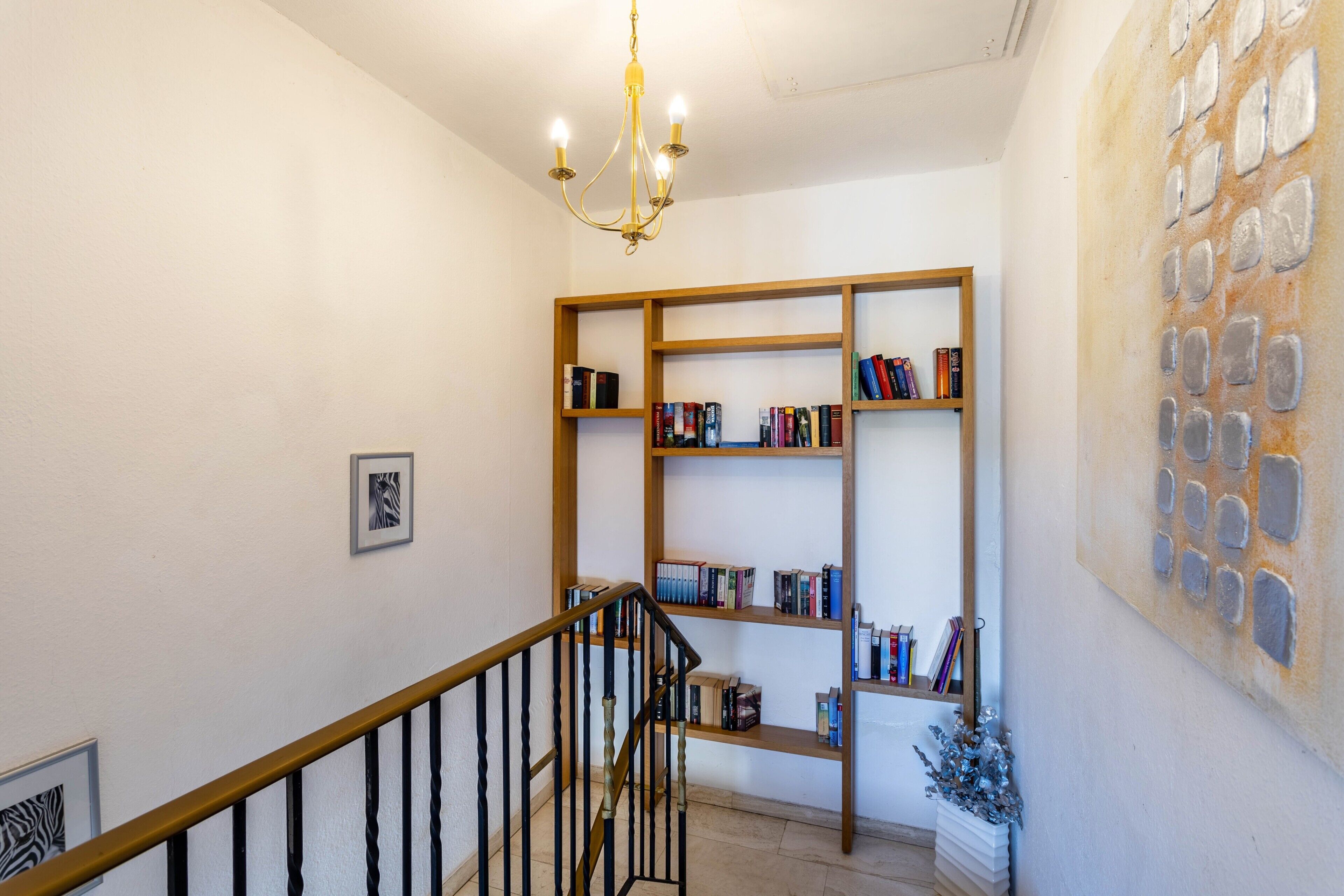 A staircase with a wooden railing, a chandelier, and a bookshelf with books.