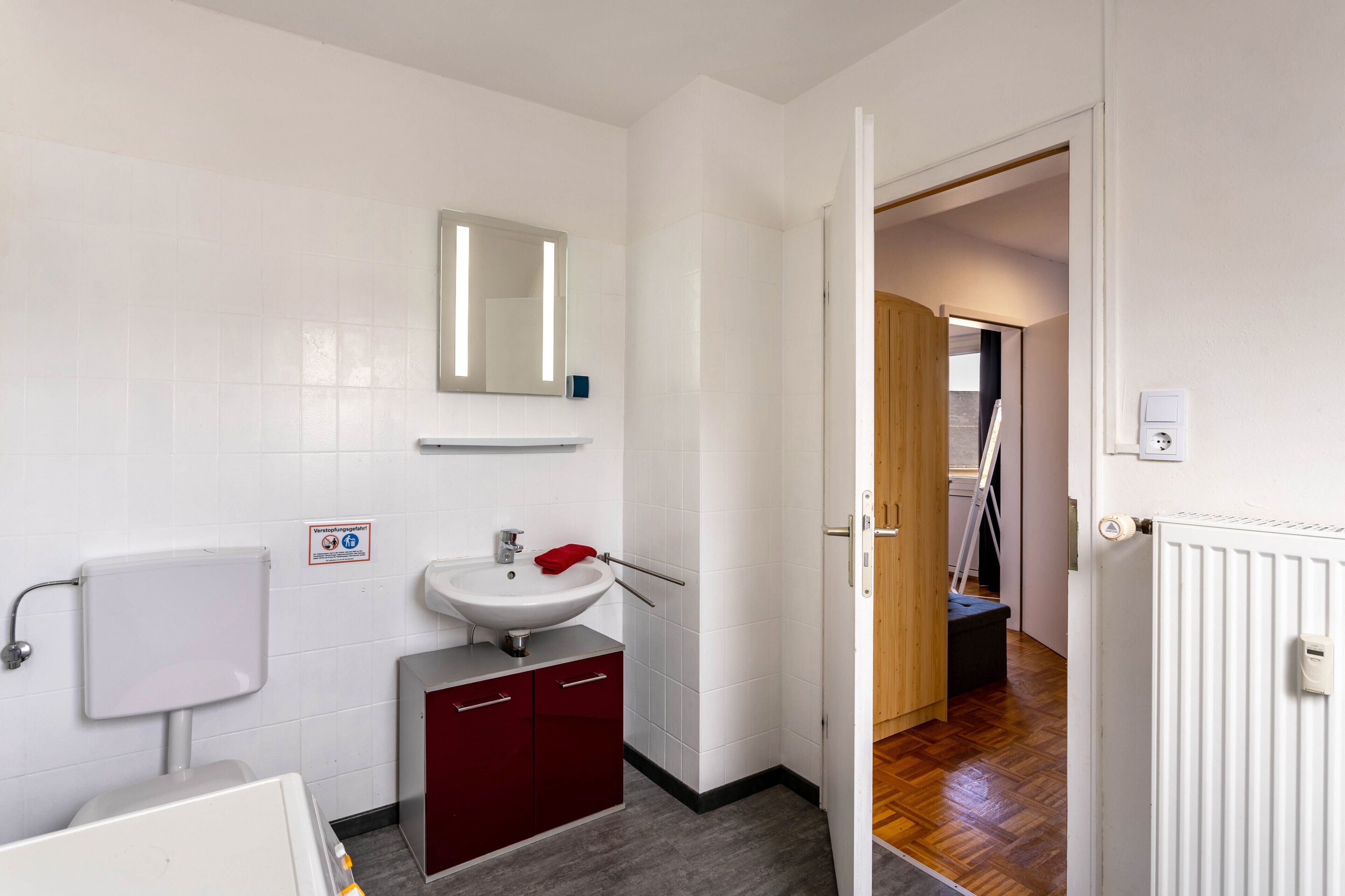Ein Badezimmer mit einem weißen Waschbecken, einem Spiegel und roten Schränken.