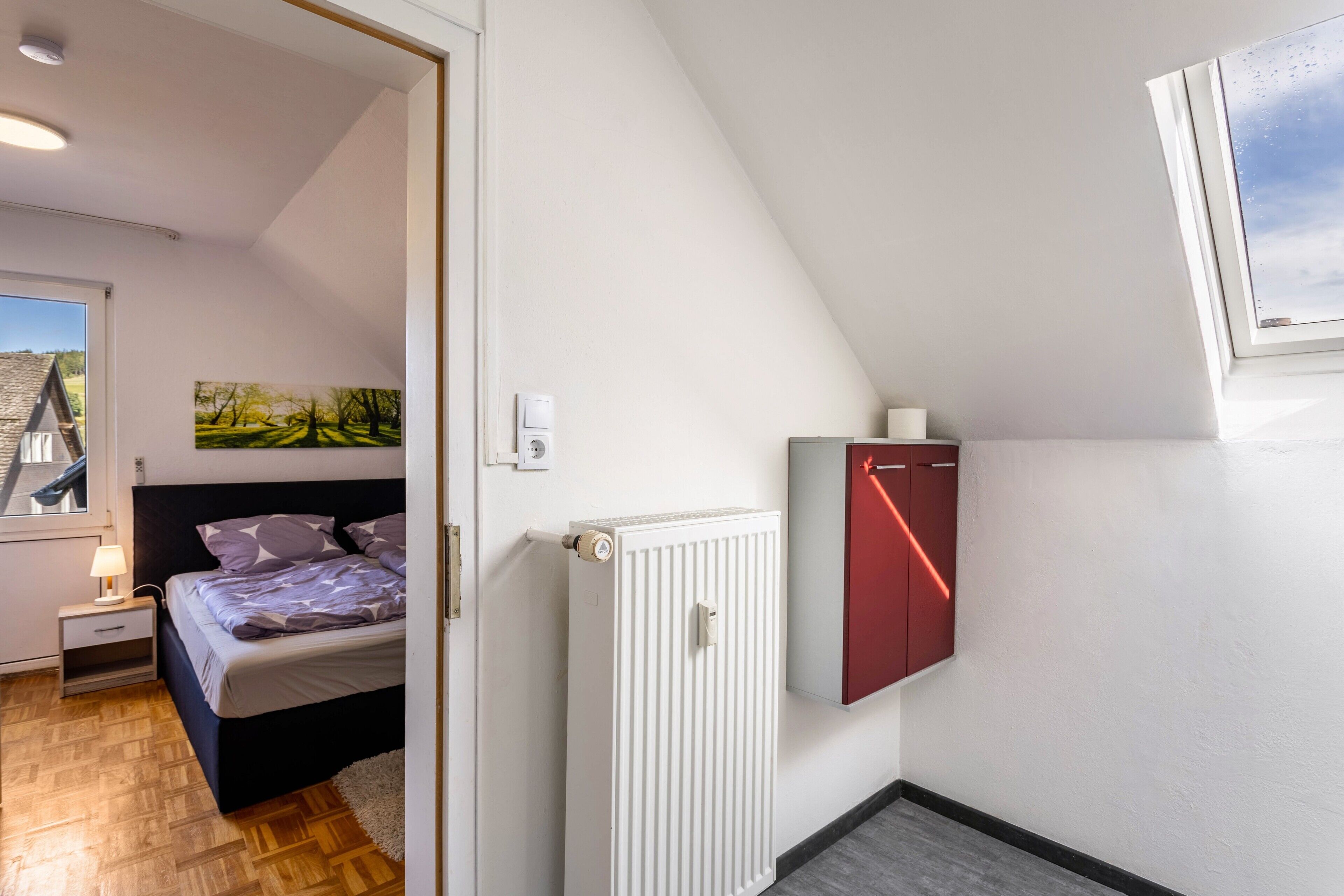 Une chambre à coucher avec un lit, une table de chevet, un radiateur et une fenêtre donnant sur un beau paysage.