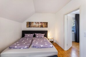 A bedroom with a bed, a nightstand, a wall-mounted picture, and a door leading to another room.