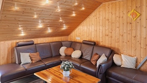 Ein Zimmer mit Holzwandverkleidung, einem braunen Ledersofa und einem Holztisch. An der Wand hängt eine Uhr.