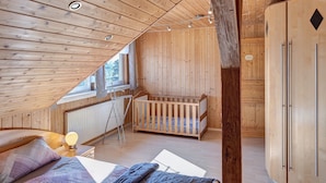 Ein Zimmer mit Holzwänden und schrägem Dach, einem Kinderbett, einem Kleiderschrank und einer Heizung.