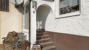 Ein Gebäudeeingang mit einer Bank, einem Mülleimer und einer Treppe.