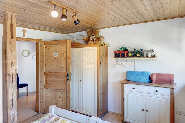 Una habitación de madera con una cama, un armario, un estante con juguetes y una silla.