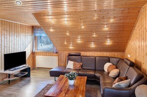 Een kamer met houten lambrisering, een leren bank, een televisie op een standaard en een raam met uitzicht.
