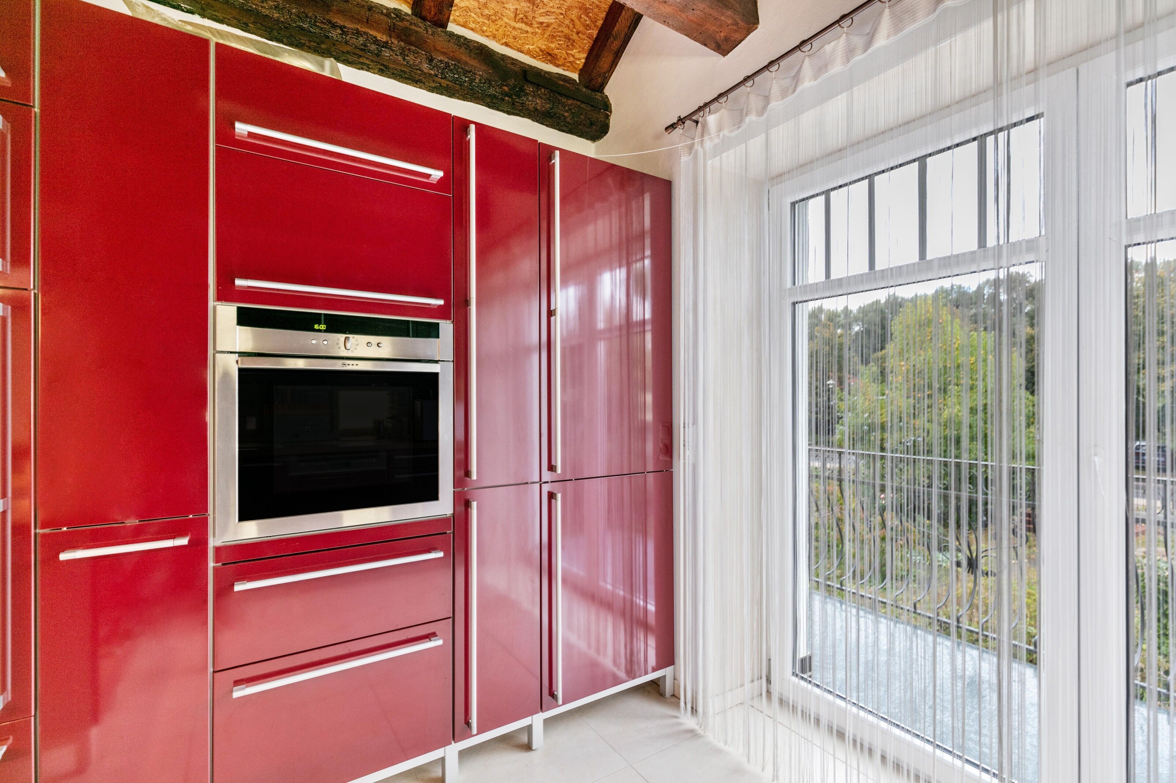 Une cuisine avec des meubles de couleur rouge, un four en acier inoxydable et une fenêtre donnant sur un paysage verdoyant.