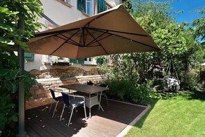 Eine Terrasse im Freien mit Tisch, Stühlen, einem großen Sonnenschirm und einer Steinmauer.