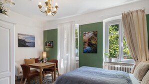 Un dormitorio con cama, un escritorio, sillas, una araña de cristal y obras de arte en las paredes.