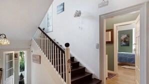 Una escalera con barandilla de madera y paredes blancas que conduce a un dormitorio con cama y pared verde.