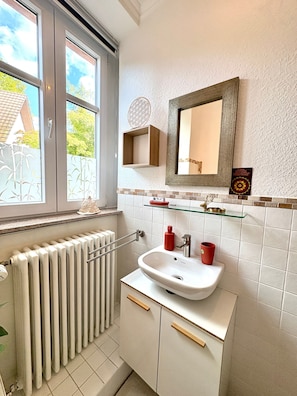 Baño con ventana, radiador, lavabo y detalles decorativos.