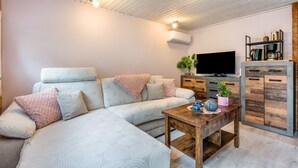 A modern living room with a sectional sofa, a wooden coffee table, a flat-screen TV, and a built-in cabinet with shelves. - Holiday Home 'Häuschen Grau' with Private Garden and Wi-Fi (Scheibenberg)