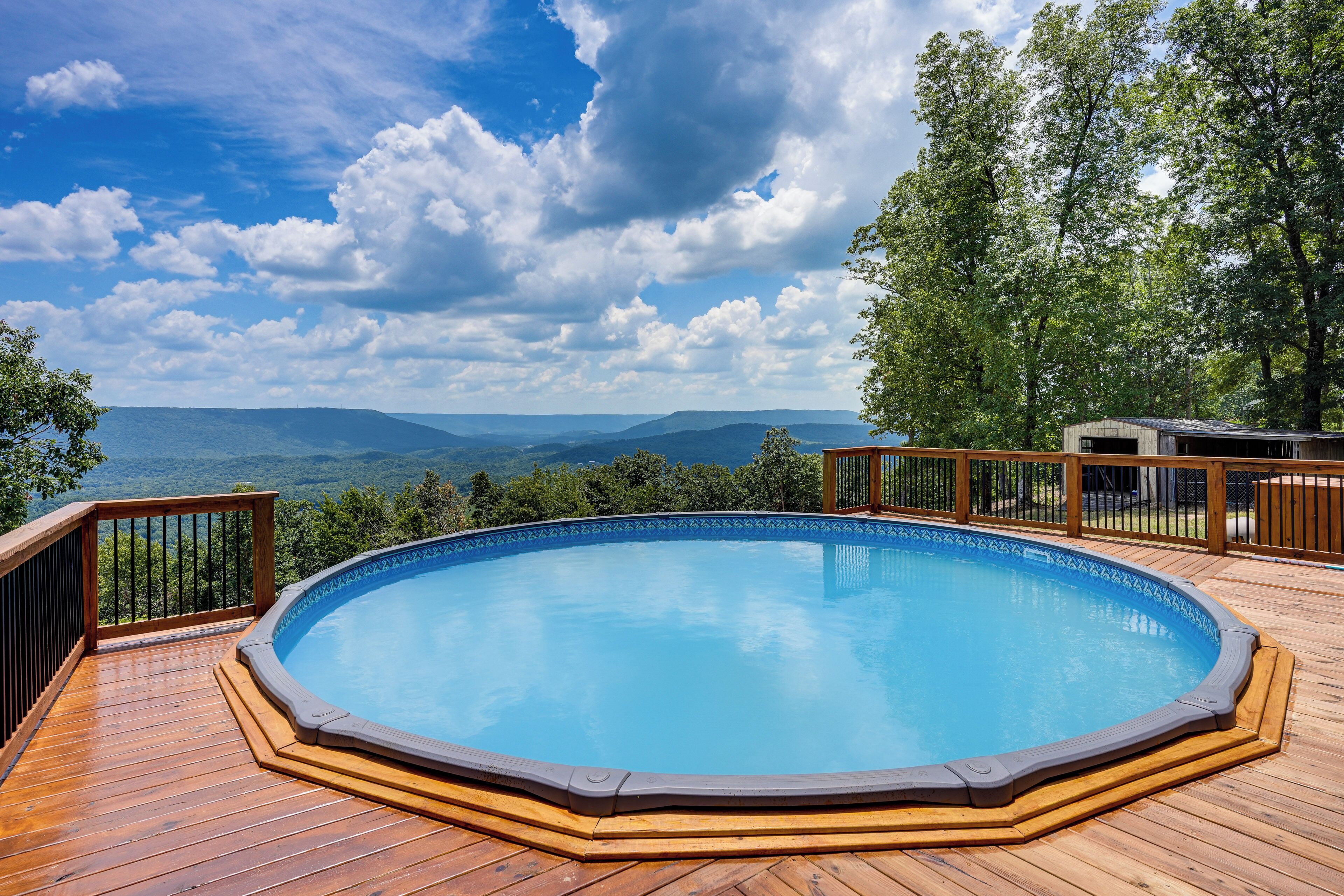 Un terrazzo in legno con piscina, circondato da alberi e una vista panoramica sulle montagne.