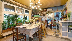 Un comedor con una mesa dispuesta para cuatro personas, rodeada de sillas de madera, una zona de bar con taburetes y vistas a la cocina a través de una ventana.