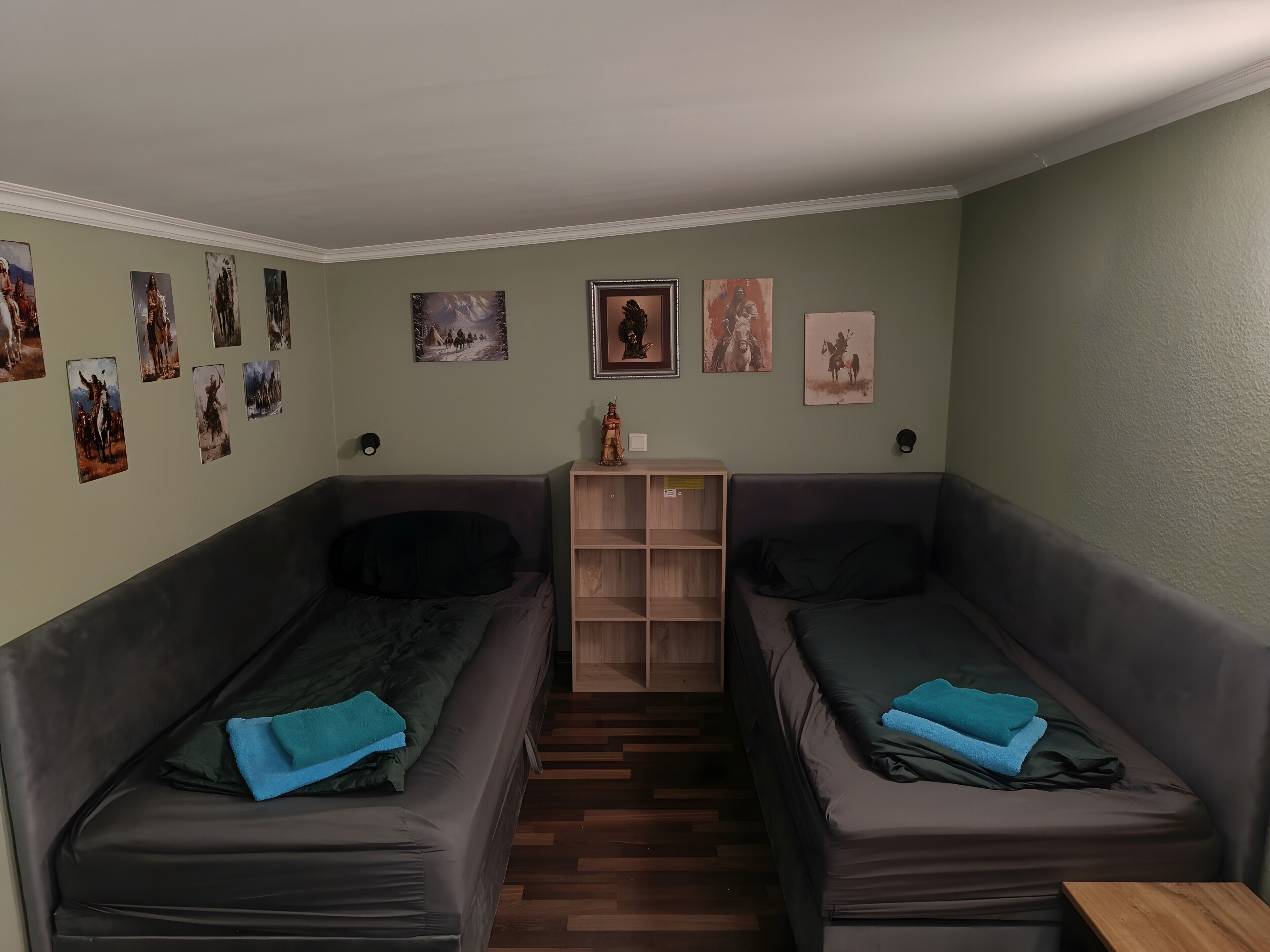Een kamer met twee donkergrijze banken, een klein houten kastje en een wand versierd met diverse ingelijste foto’s.