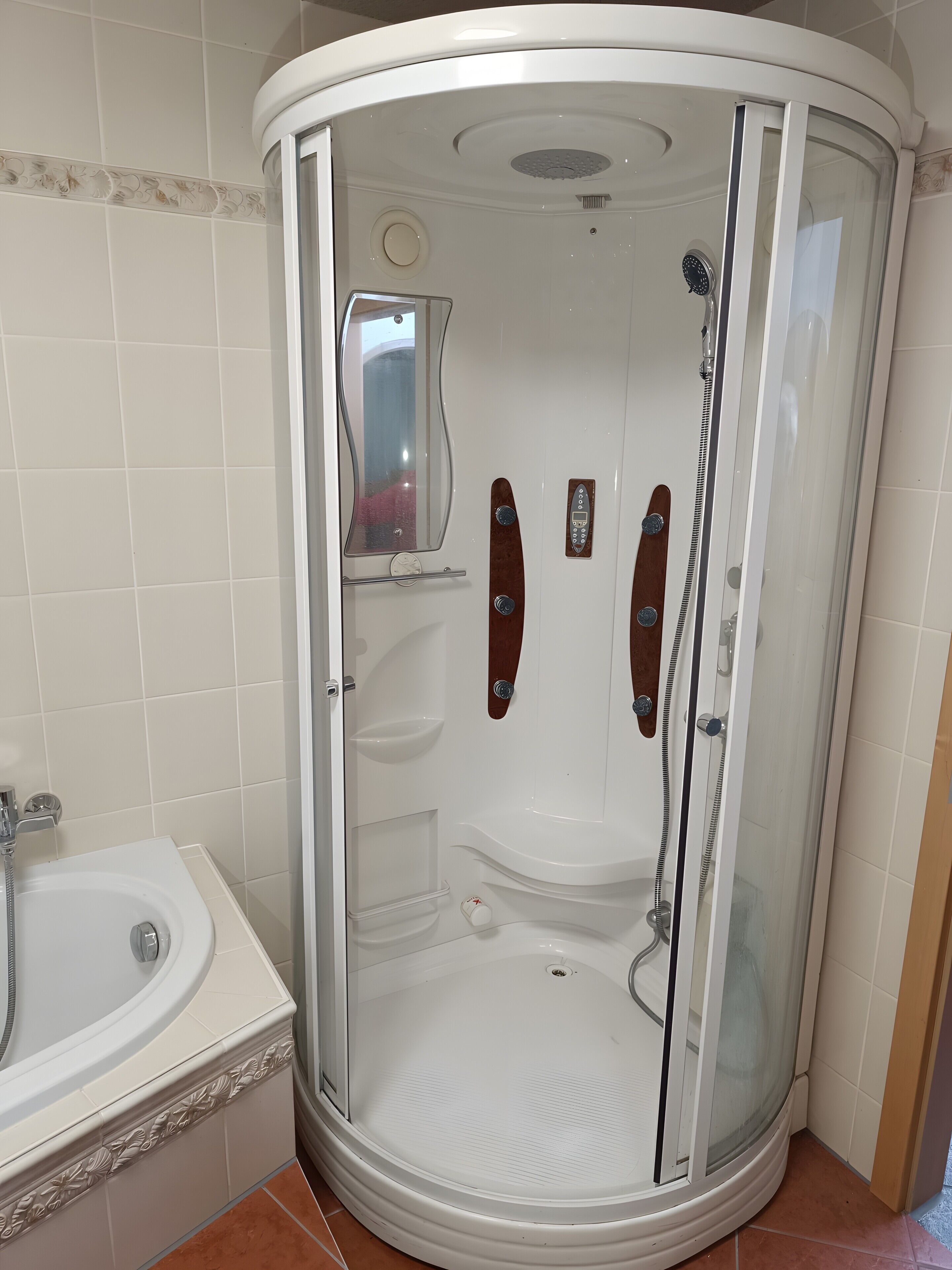 Un espace de douche d’angle doté d’une porte en verre, d’un banc intégré et d’un panneau de commande.