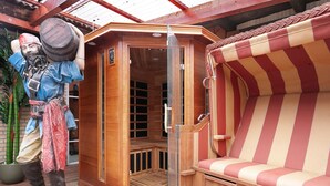 Una sauna de madera con puerta de vidrio, un banco a rayas y una estatua de un hombre con un barril.