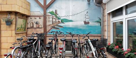Bicicletas estacionadas em frente a um edifício com um mural de paisagem costeira.