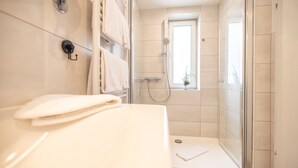 Un baño moderno con cabina de ducha de vidrio, lavamanos blanco y ventana que proporciona luz natural.