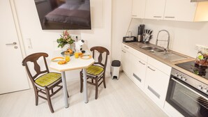 Una cocina compacta con una mesa de comedor, sillas, un televisor sobre la mesa, un lavamanos y un horno.