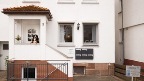 Un edificio blanco con techo de tejas rojas, el número '5' en la puerta, un pequeño balcón con un perro y un cartel que dice 'LANDGRAF'.