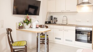 Una cocina moderna con armarios blancos, horno empotrado, televisor de pantalla plana y comedor con mesa y sillas.