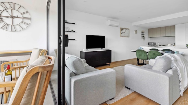 A modern living room with a sofa, a TV, and a dining area with chairs.