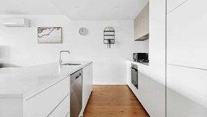 A modern kitchen with white cabinetry, a dishwasher, a microwave, and a clock on the wall.