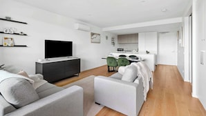 A modern living room with a sofa, a TV, and a dining area with chairs.