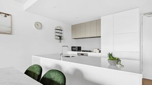 A modern kitchen with white cabinetry, a central island, a microwave, and a clock on the wall.