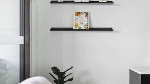 A modern room with a bed, a window, and three black shelves with decorative items.