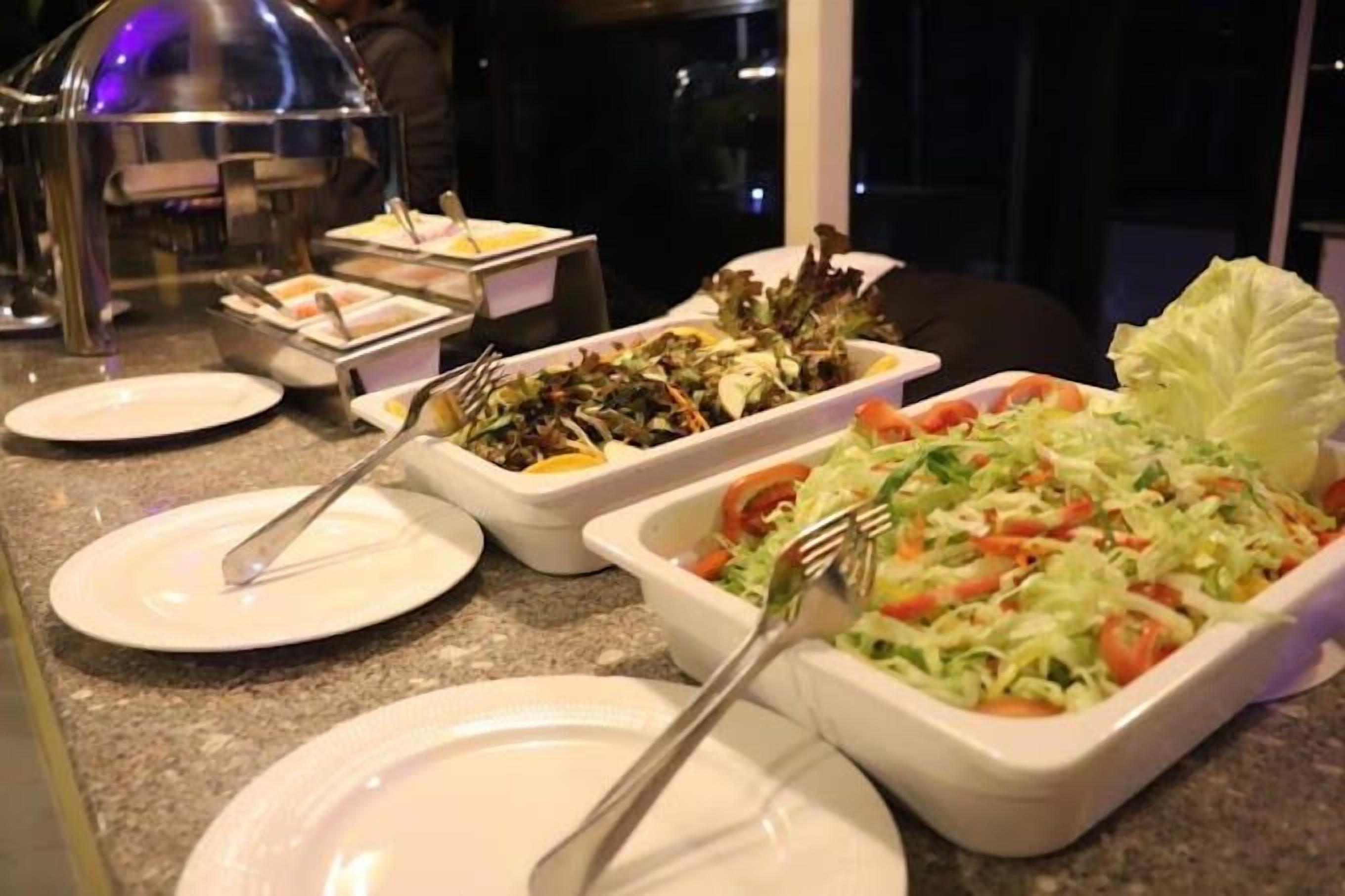 A buffet setup with various dishes including salads and possibly some cold cuts, served on white plates and trays.