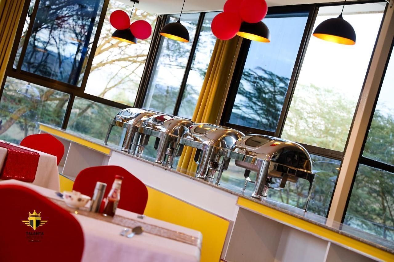 A dining area with a row of espresso machines, a table with a red chair, and a view of trees through large windows.